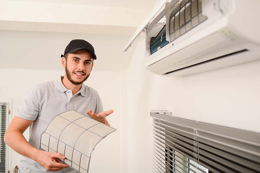 handsome young man electrician cleaning air filter on an indoor unit of air conditioning system in a client house AC Efficiency and AC Repair