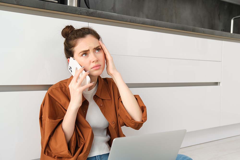 Portrait of woman calling her doctor on the phone, holding smartphone, frowning and touching her head, has painful headache or migraine, feeling unwell